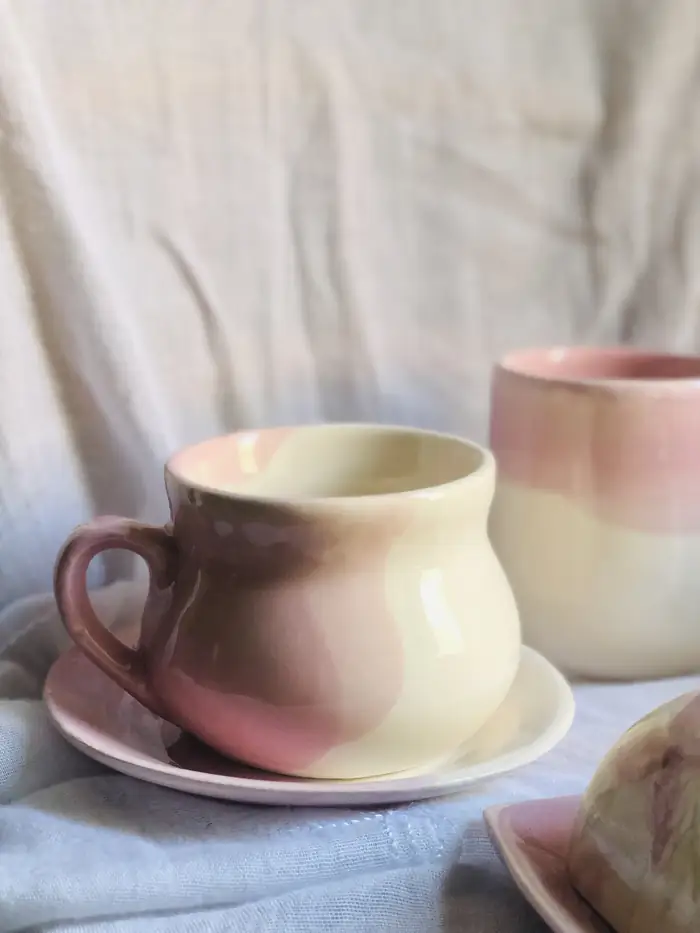 Taza y mantequera de cerámica artesanal en rosa empolvado sobre lino